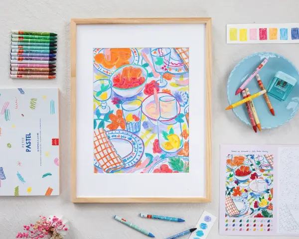 Un dessin pastel facile à faire d'une table de pique-nique colorée, entouré de pastels, d'une boîte et d'un livre de coloriage.