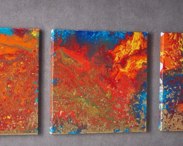 Trois toiles abstraites aux couleurs vives, un exemple de pouring art, avec des touches dorées.