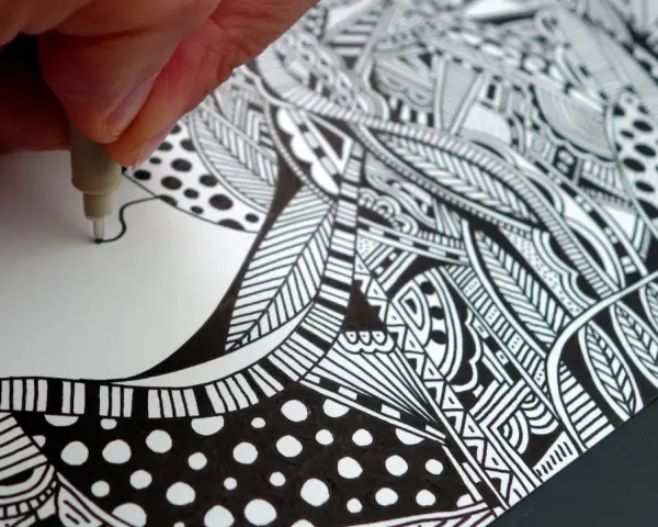 Main d'artiste créant un gribouillage artistique complexe, rempli de motifs géométriques et organiques en noir et blanc.