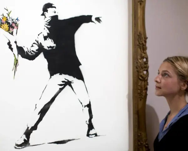 Une jeune femme admire "Flower Thrower", une œuvre emblématique de qui est Banksy, représentant un homme lançant un bouquet de fleurs.