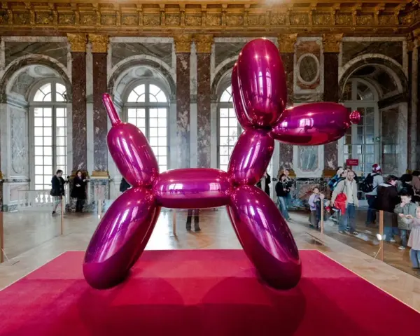 Une sculpture de chien ballon rose vif, une des œuvres d'art de Jeff Koons, trône sur un tapis rouge dans un grand hall orné.