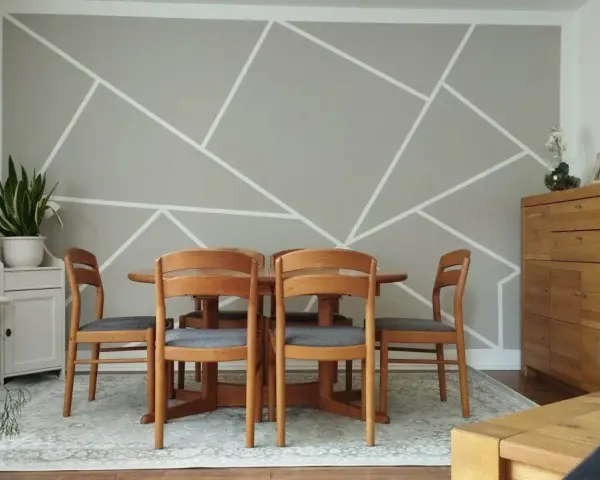 Un salon moderne avec un motif décoration peinture géométrique sur le mur. Une table en bois et des chaises grises sont disposées au centre.