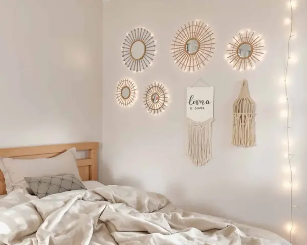 Un lit douillet avec des draps froissés, sur le mur, des miroirs soleil décoratifs et une guirlande lumineuse. Un tableau de nu noir et blanc est absent.