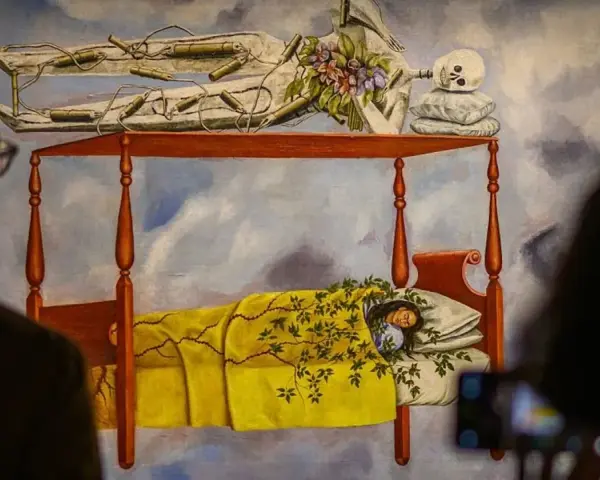 La peinture de Frida Kahlo "Le lit volant" montre une femme endormie sous une couverture jaune, avec un squelette au-dessus.
