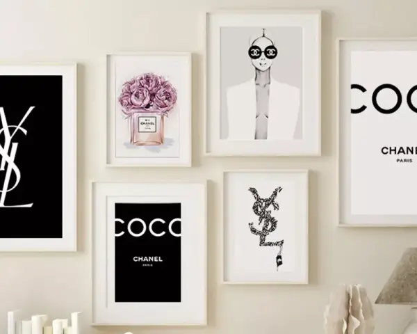 Un mur décoré de plusieurs tableaux, dont un tableau metal vintage avec le logo YSL noir sur fond noir, et des affiches Chanel.