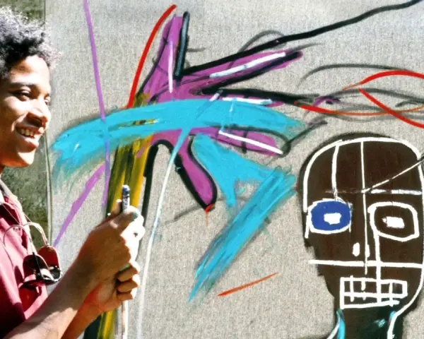 Un jeune homme souriant crée une œuvre d'art vibrante dans un style Basquiat, avec des couleurs vives et des formes audacieuses.