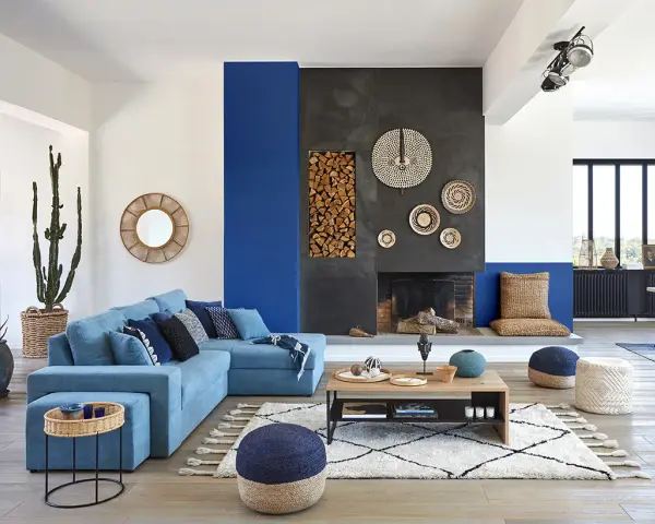 Un salon moderne avec un grand canapé bleu, une cheminée imposante et un tableau bleu marine sur le mur.