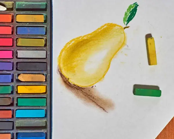 Une boîte de pastels secs pour débutant, avec une poire jaune esquissée sur du papier blanc, et des pastels jaune et vert à côté.