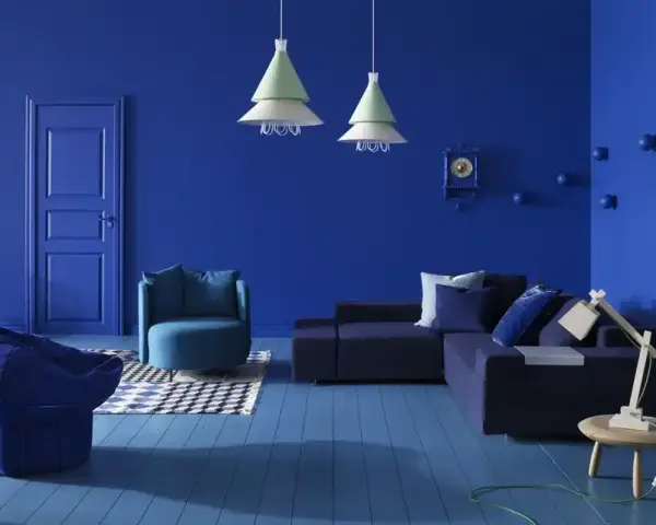 Un salon moderne aux murs et au sol bleu profond. Un canapé d'angle, un fauteuil, un pouf et une table basse complètent ce tableau déco bleu.