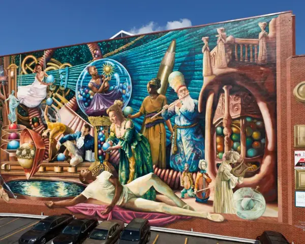 Fresque colorée représentant des personnages historiques et mythologiques, un artiste engagé qui dépeint la richesse culturelle.