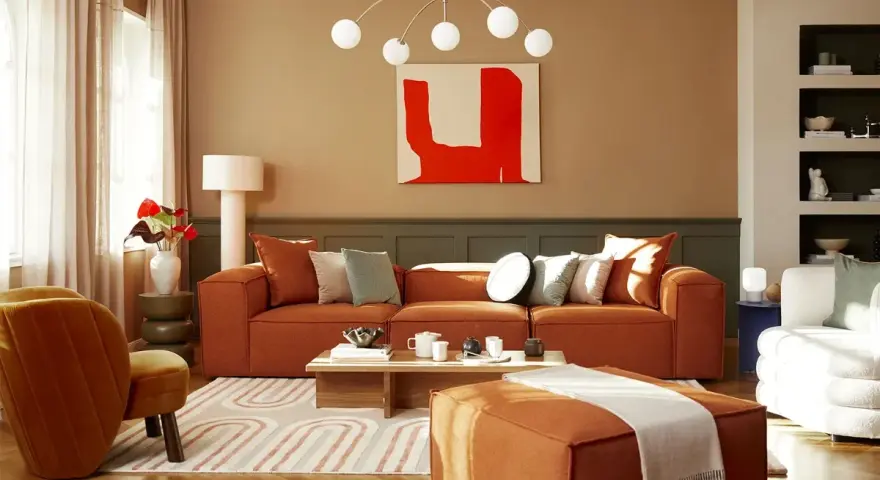 Salon cosy avec canapé orange, fauteuil velours et un tableau couleur chaude.
