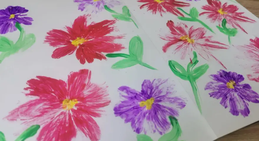 Des fleurs peintes en relief, rouges et violettes, avec des touches de jaune au centre. Une technique simple pour apprendre comment peindre des fleurs en relief.