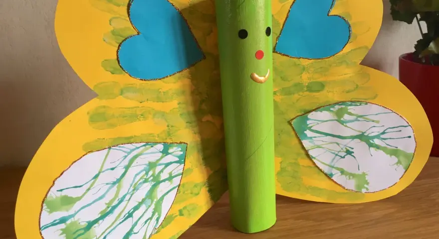 Papillon jaune aux ailes décorées de peinture à la paille, avec un corps vert en rouleau de papier toilette.