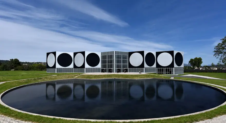 Le Centre d'art contemporain de Vassivière, avec ses façades ornées de cercles noirs et blancs, reflète les œuvres d'art de Victor Vasarely dans un étang paisible.