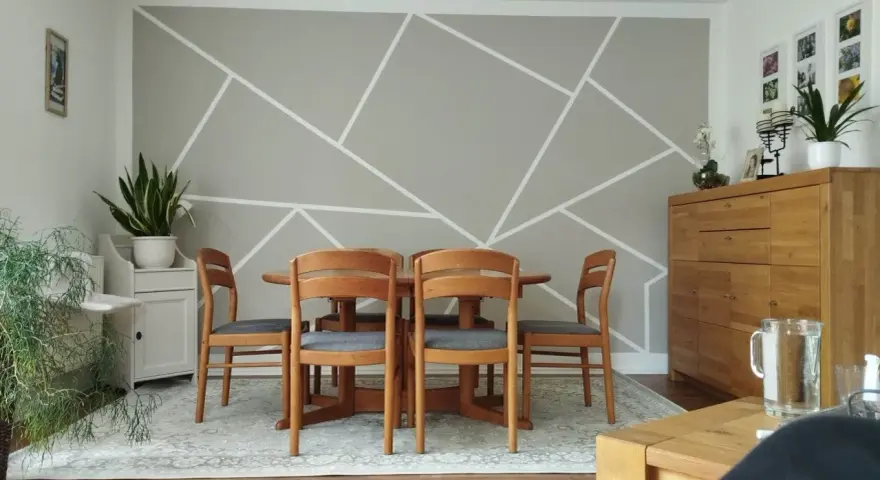 Un salon moderne avec un motif décoration peinture géométrique sur le mur. Une table en bois et des chaises grises sont disposées au centre.