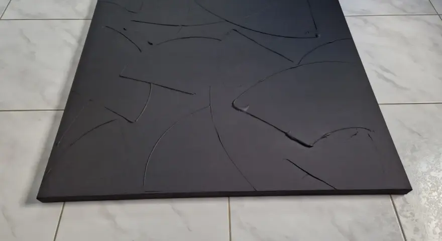 Une toile texturée, d'un noir absolu, aux courbes abstraites et profondes, posée sur un sol carrelé.