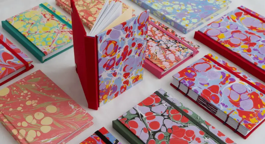 Collection de carnets aux motifs marbrés colorés, évoquant le motif Annonay. Des couleurs vives et des formes organiques se mélangent sur les couvertures.
