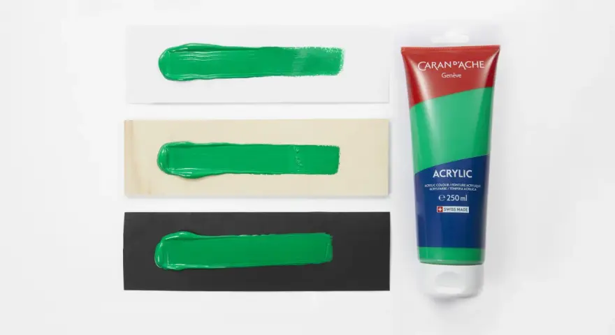 Bandeaux de peinture verte sur papier blanc, bois et noir, à côté d'un tube de gouache Caran d'Ache.