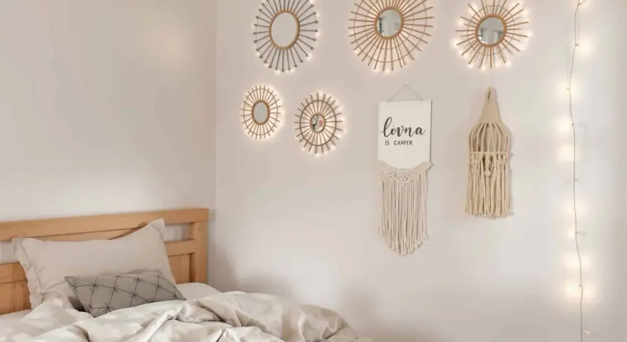 Un lit douillet avec des draps froissés, sur le mur, des miroirs soleil décoratifs et une guirlande lumineuse. Un tableau de nu noir et blanc est absent.