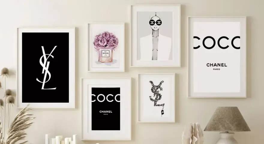 Un mur décoré de plusieurs tableaux, dont un tableau metal vintage avec le logo YSL noir sur fond noir, et des affiches Chanel.