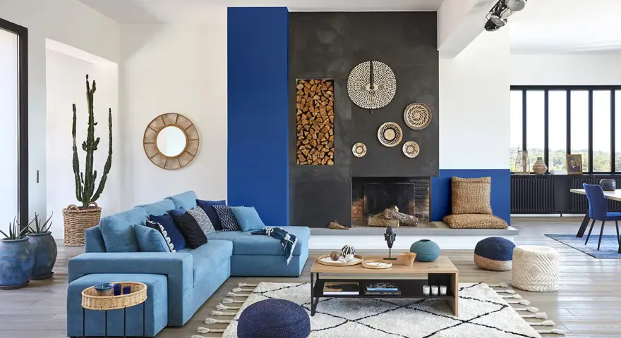 Un salon moderne avec un grand canapé bleu, une cheminée imposante et un tableau bleu marine sur le mur.