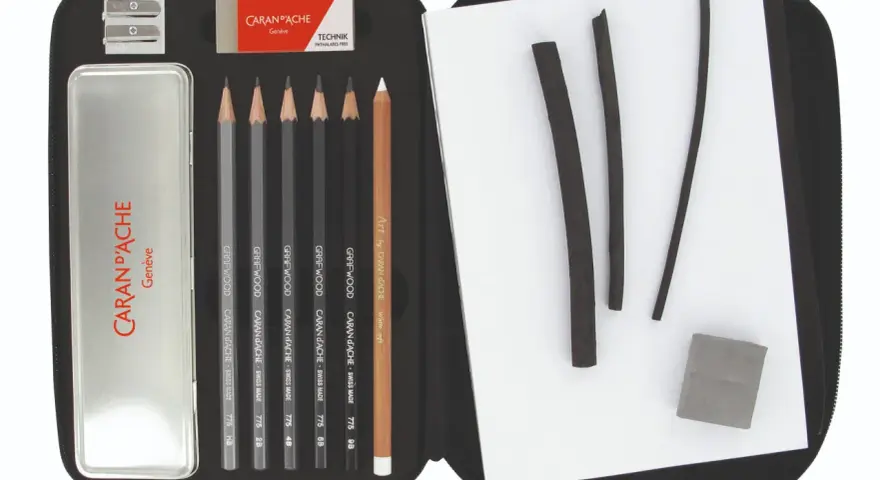 Étui ouvert révélant un matériel de dessin liste : crayons graphite, fusains, gomme et taille-crayon Caran d'Ache.