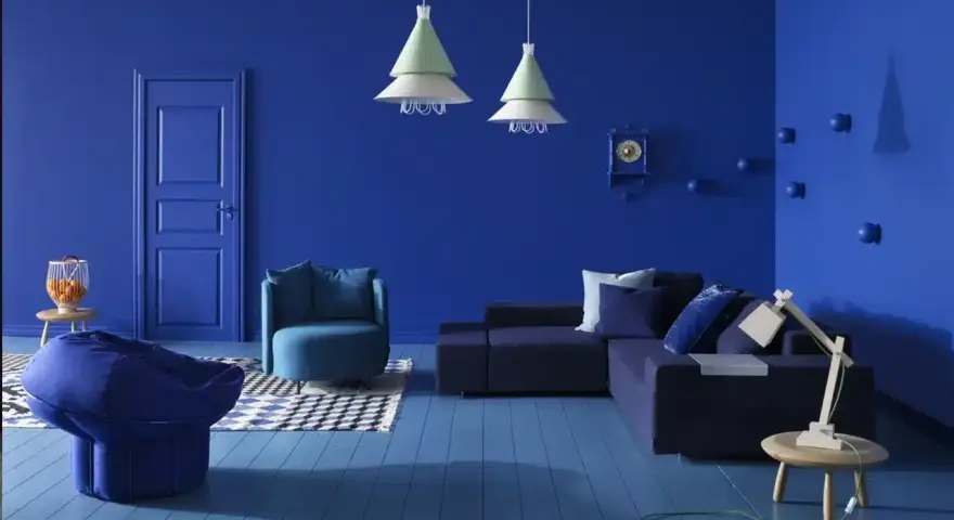 Un salon moderne aux murs et au sol bleu profond. Un canapé d'angle, un fauteuil, un pouf et une table basse complètent ce tableau déco bleu.