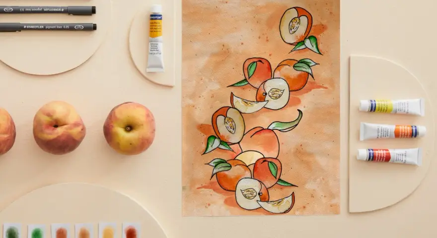 Une peinture de fruit aquarelle, avec des pêches entières et coupées, des tubes de peinture et des feutres.