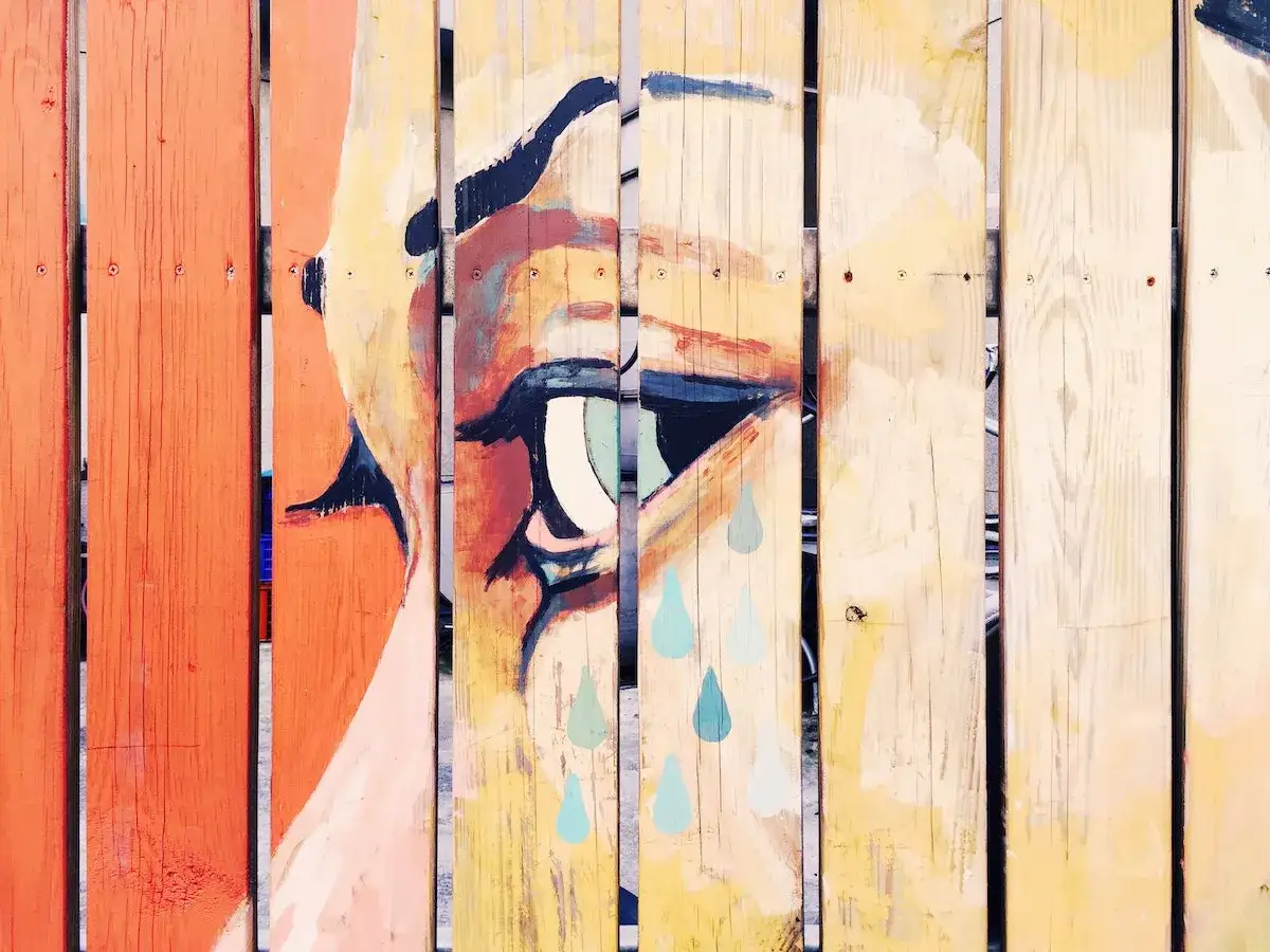 &OElig;uvre d'un artiste peintre sur bois : un &oelig;il expressif aux larmes bleues sur une cl&ocirc;ture en planches.