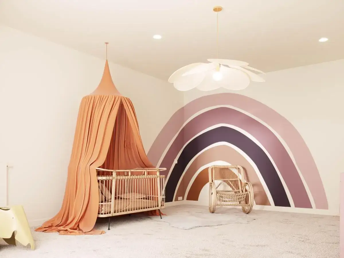 Chambre d'enfant avec un arc-en-ciel peint fait maison sur le mur, un berceau orange et un fauteuil en rotin.