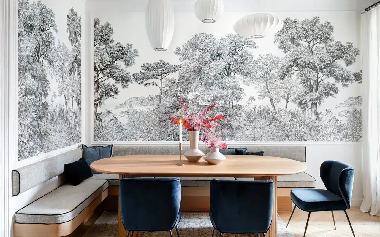 Un tableau panoramique noir et blanc orne le mur d'une salle &agrave; manger, repr&eacute;sentant une for&ecirc;t luxuriante. Une banquette grise et des chaises bleues compl&egrave;tent l'ensemble.
