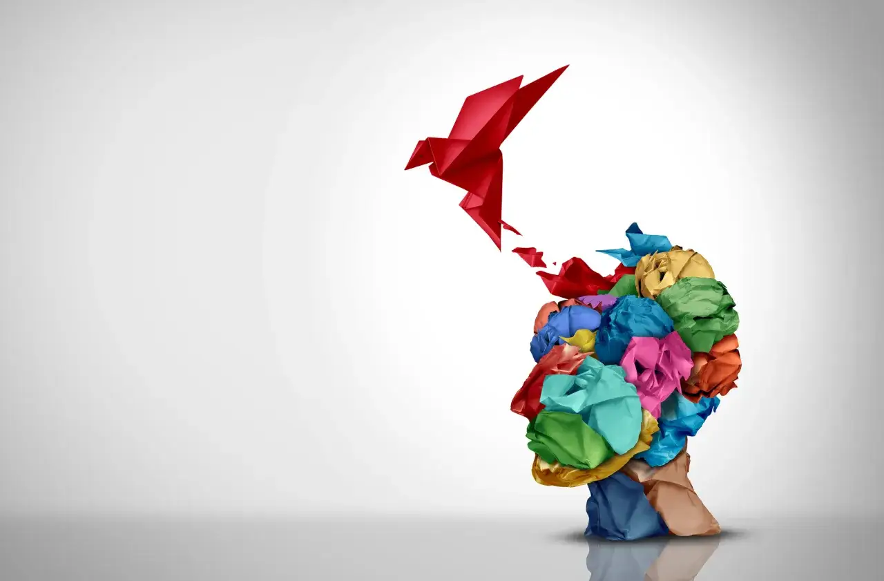 Une tête formée de papier froissé multicolore libère un oiseau rouge en origami, symbole de créativité artistique.