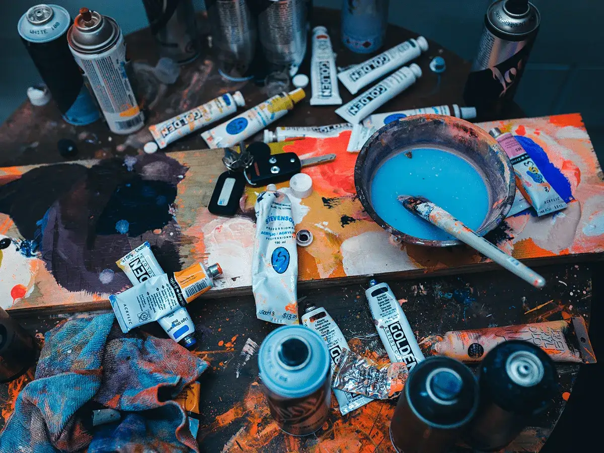 Sur une palette éclaboussée, des tubes de peinture acrylique, des bombes aérosols et un pinceau trempé dans du bleu attendent le prochain coup de génie.