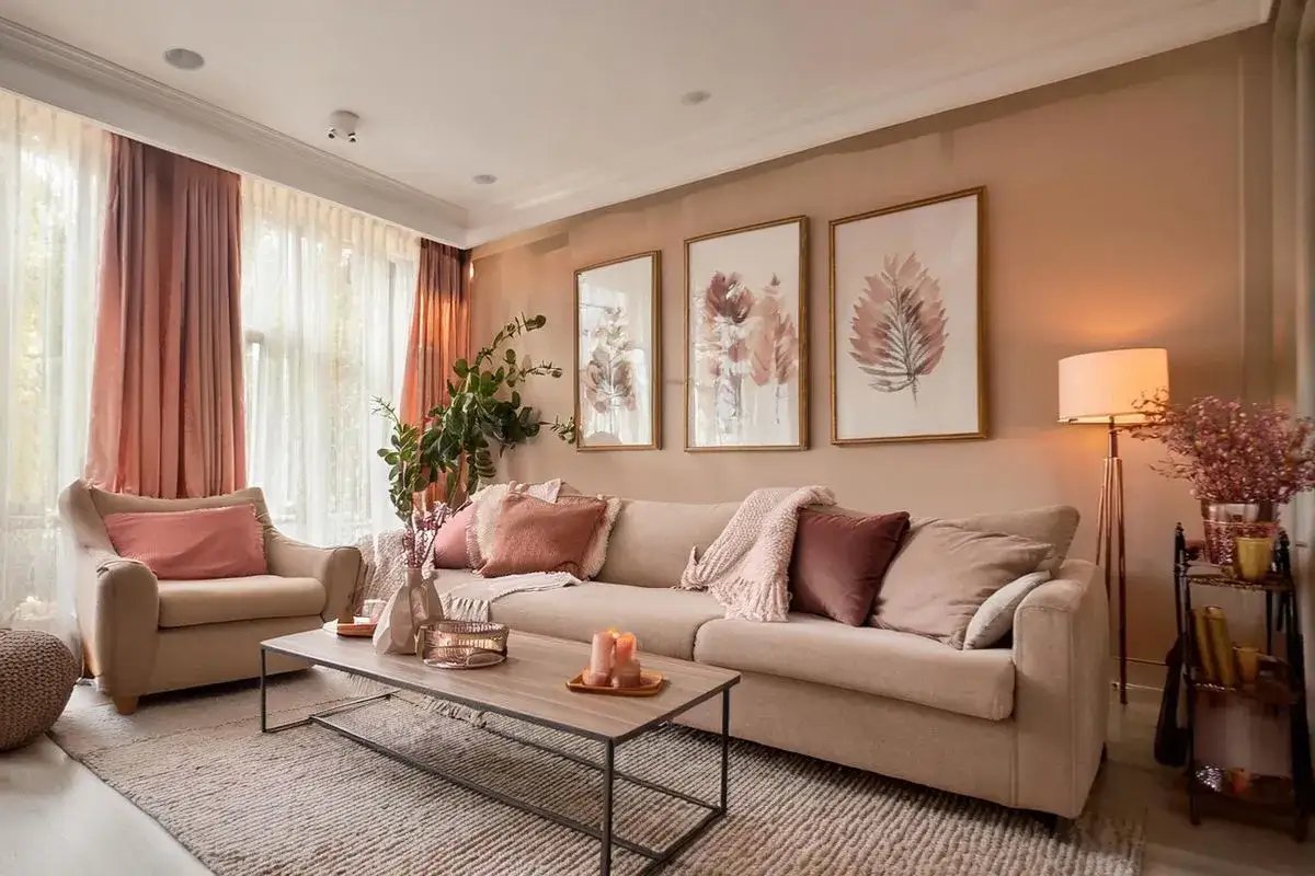 Un salon cosy avec un canap&eacute; beige, des coussins roses et un tableau couleur chaude.