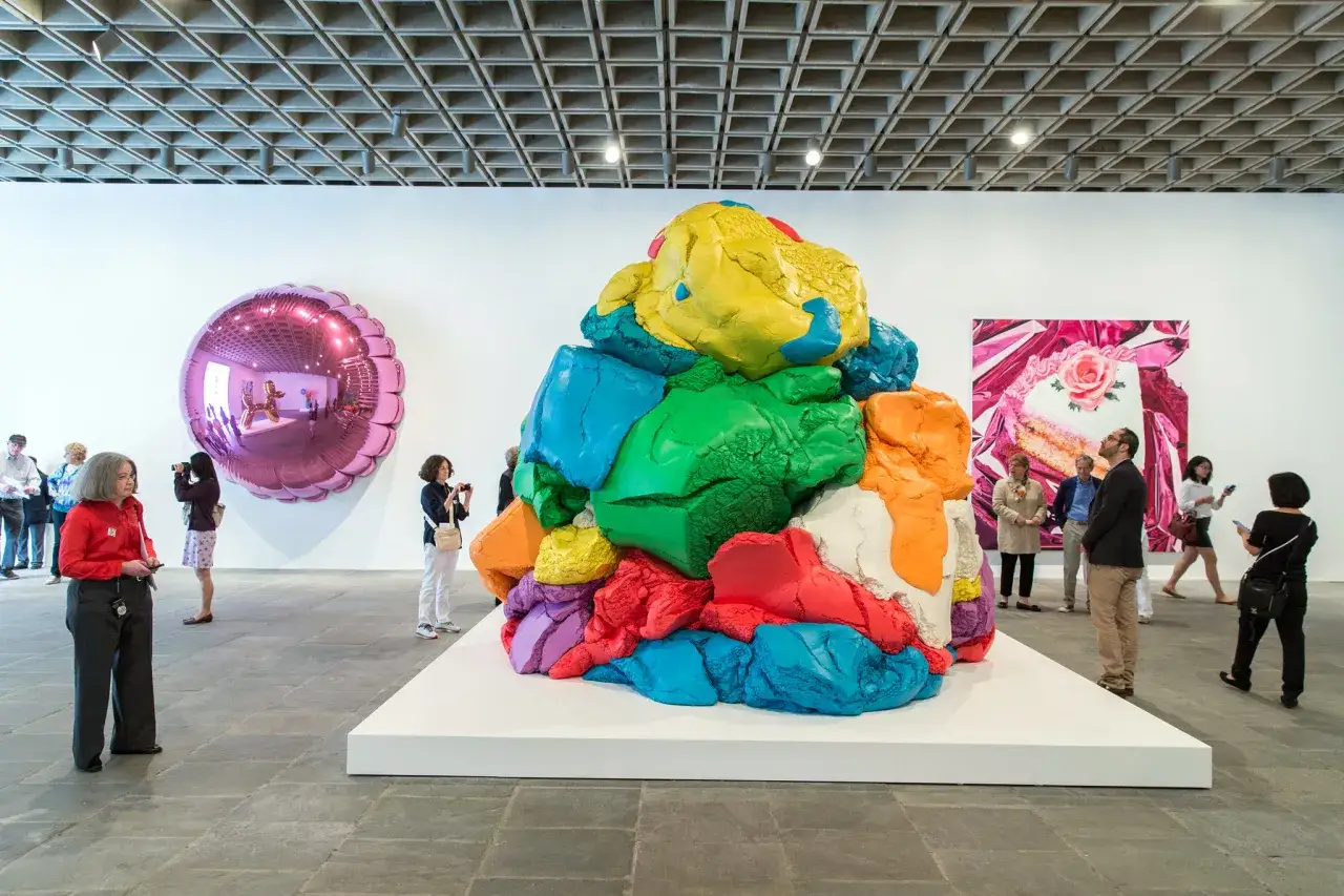 Des &oelig;uvres d'art de Jeff Koons dans une galerie : une sculpture color&eacute;e en p&acirc;te &agrave; modeler, un ballon gonflable rose et une peinture de g&acirc;teau.