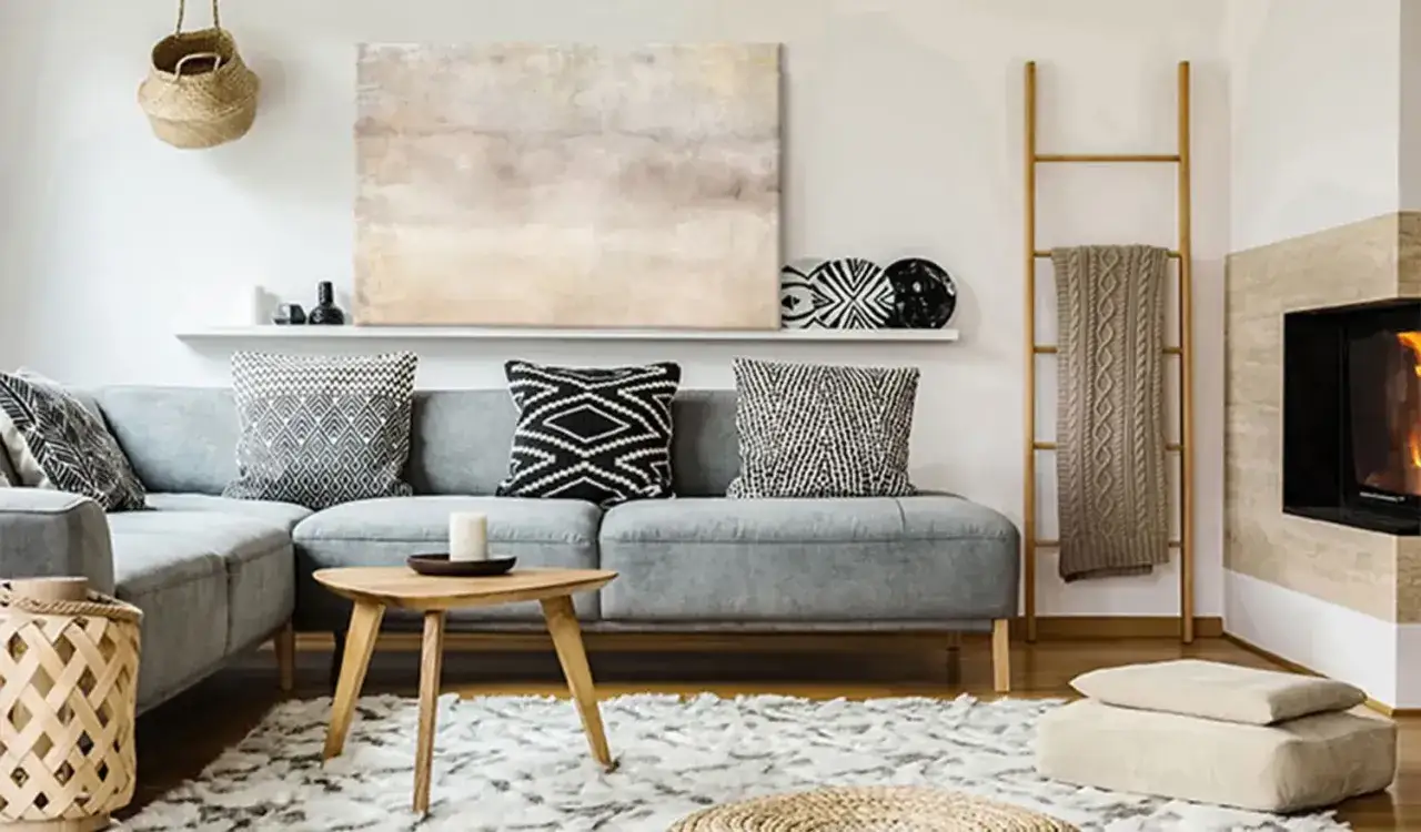 Un salon cosy avec un grand tableau beige abstrait au-dessus d'un canap&eacute; gris, des coussins graphiques et une chemin&eacute;e.