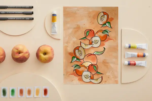 Une peinture de fruit aquarelle, avec des pêches entières et coupées, des tubes de peinture et des feutres.