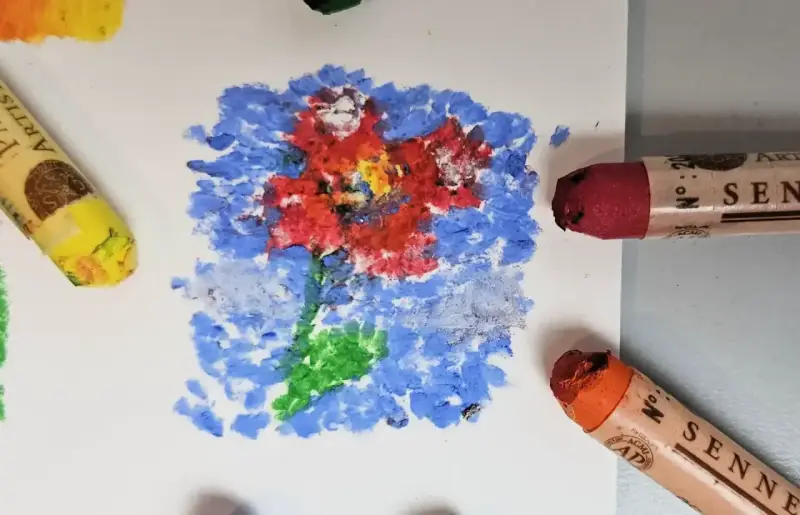 Apprenez comment utiliser les pastels à l'huile pour créer une fleur vibrante sur fond bleu. Des pastels jaune, rouge et orange sont visibles.