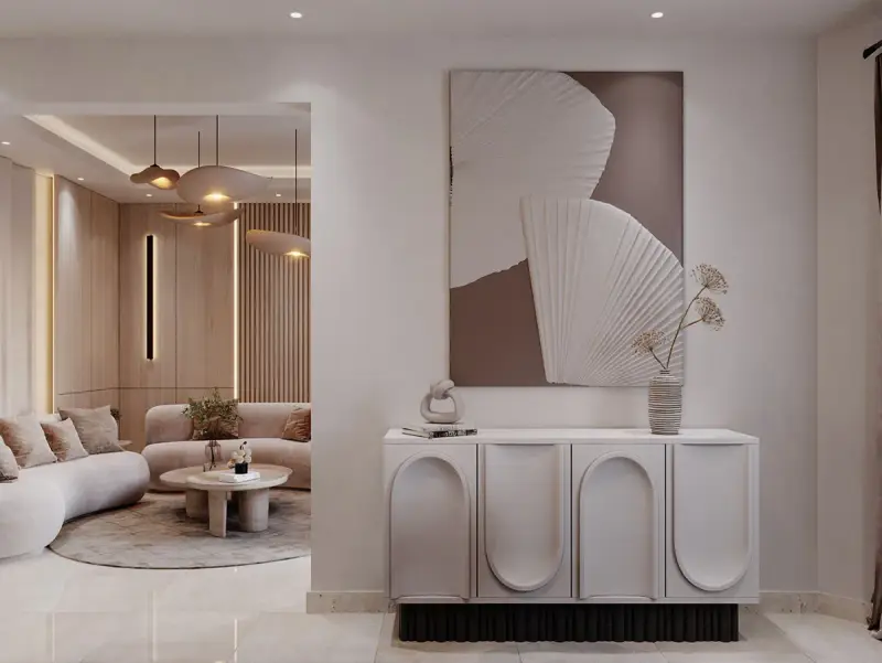 Un tableau marron beige abstrait orne un mur au-dessus d'un buffet moderne. Le salon adjacent est baigné de lumière douce.