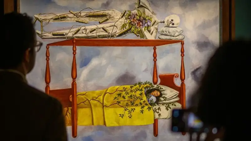 La peinture de Frida Kahlo "Le lit volant" montre une femme endormie sous une couverture jaune, avec un squelette au-dessus.